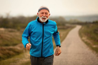 Happy senior athletic man feeling motivated while listening music and running in nature in the morning. Copy space. 