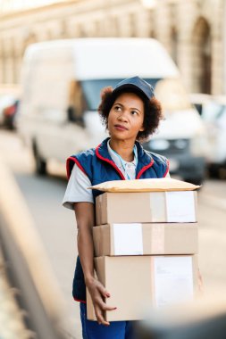 Young happy manual worker carrying cardboard boxes