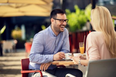 Cheerful man talking to his girlfriend who is using mobile phone in a cafe.