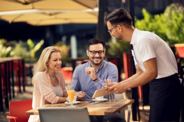 Smiling couple holding hands and enjoying in a cafe while waiter is showing them menu on digital tablet.