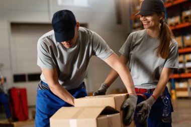 Male worker assisting his female colleague with cardboard boxes while working in a warehouse. 