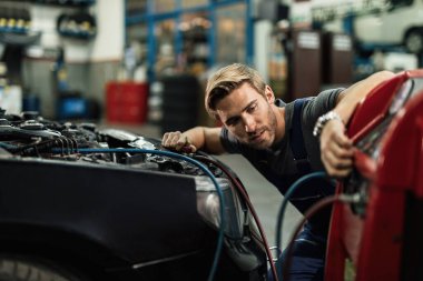 Young auto mechanic using compressor while maintaining AC unit of a car at workshop. 