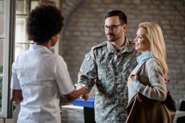 Happy military couple shaking hands with African American doctor after counselling at the clinic. 