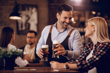 Happy waiter having fun while serving beer and talking to a female customer in a bar. 