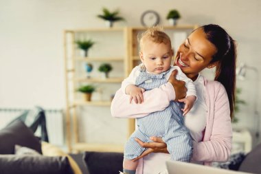 Happy mother enjoying while holding her baby son and spending time with him at home. 