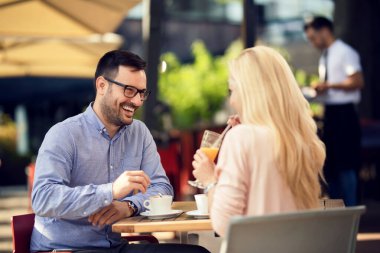 Happy man and his girlfriend talking to each other while spending time together in a cafe. 
