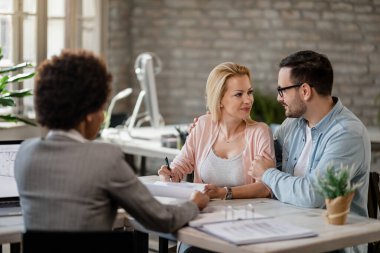 Smiling couple talking while woman is signing a contract during the meeting with insurance agent in the office. 