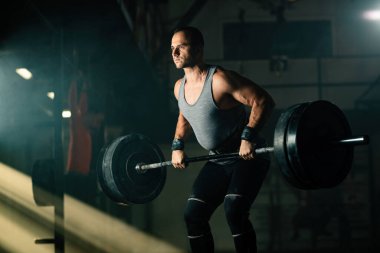 Athletic man exercising with barbell during cross training in health club. 