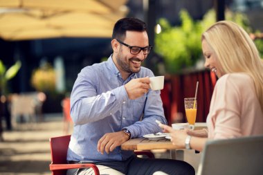 Happy man drinking coffee and having fun with his girlfriend while she is using cell phone in a cafe. 