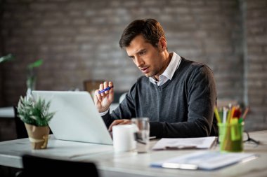 Concentrated businessman going through project very carefully while working on a computer in the office. 