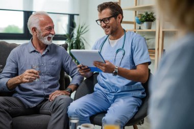 Happy senior man talking with a doctor who is reading medical reports during home visit. 