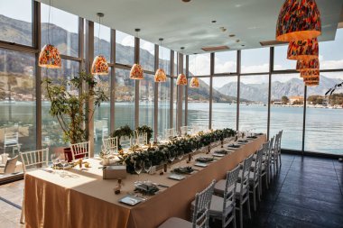 Elegantly decorated table setting in weeding reception hall with view at the sea. 