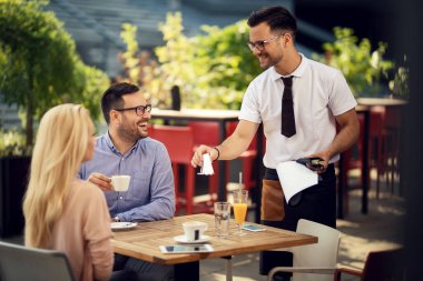 Happy waiter giving napkins to a couple while preparing their table for dining in a restaurant. 