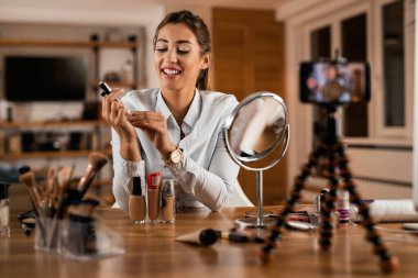 Happy make-up artist recording video tutorial about beauty products for her vlog at home. 