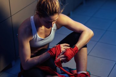 High angle view of female fighter preparing for exercising and wrapping hands with bandages in locker room. 