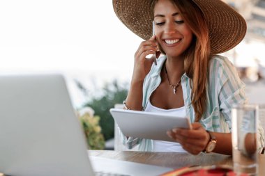 Happy woman communicating on smart phone while using digital tablet in a cafe. 