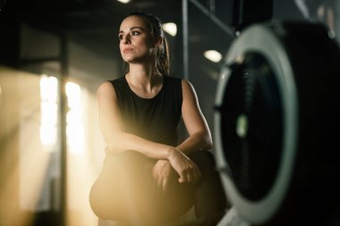 Young athletic woman resting after exercising on rowing machine in a gym.