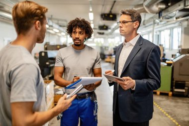Serious supervisor and metal workers talking while performing quality control check in a factory. 