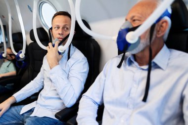 Two men communicating while having hyperbaric oxygen therapy at clinic. Focus is on mid adult man. 