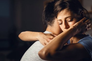 Young distraught woman with eyes closed being embraced by her boyfriend.