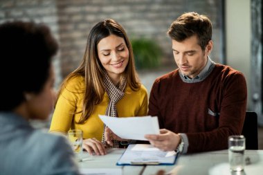 Happy mid adult couple going through paperwork and analyzing a contract on a meeting with bank manager. 