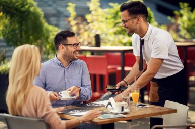 Happy couple talking to a waiter while he is setting their table for dining in a restaurant. 