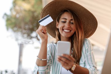 Happy woman with credit card using mobile phone and checking her bank account while relaxing in a cafe. 
