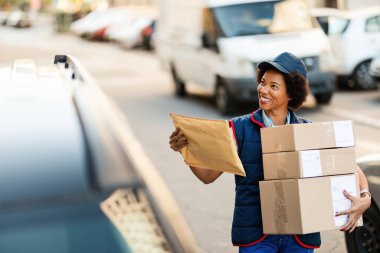 Happy African American courier carrying packages while making a delivery in the city. 