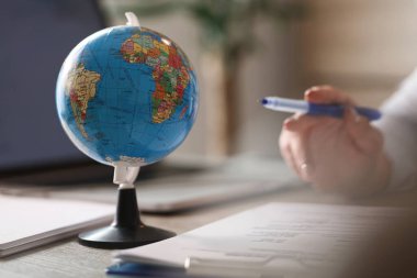 Globe on office desk with unrecognizable business person working on reports.