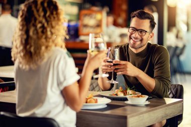 Young happy man communicating with his girlfriend while having a lunch and drinking wine in a restaurant. 