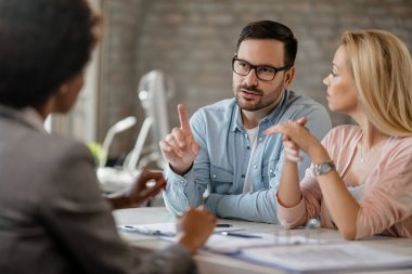 Mid adult couple communicating with insurance agent during consultations in the office. Focus is on man. 