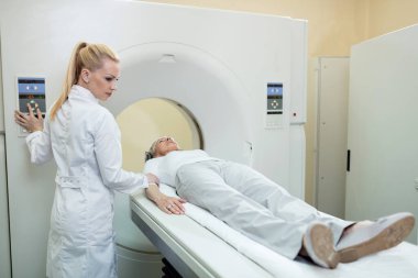 Female radiologist supervising mature patient who is undergoing for CT scan procedure in the hospital.