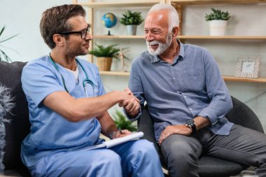 Happy senior man shaking hands with a doctor who is being in a home visit. 
