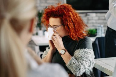 Young businesswoman suffering from a cold and blowing her nose in a tissue in the office.  