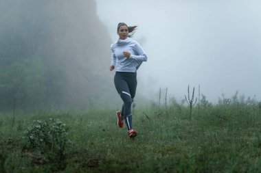 Determined athletic woman running though misty meadow during cold weather. Copy space. 