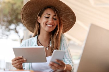 Happy woman sitting in a cafe and text messaging on mobile phone while using touchpad. 