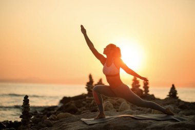 Athletic woman stretching while exercising on a beach rock at sunset. Copy space. 