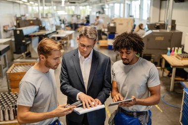 Mid adult engineer and two steel workers going through quality reports while working in industrial building. 