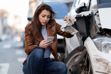 Young sad woman text messaging on smart for after a car crash on the road. 