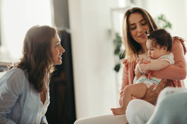 Young woman visiting a female friend and her baby daughter at home. 