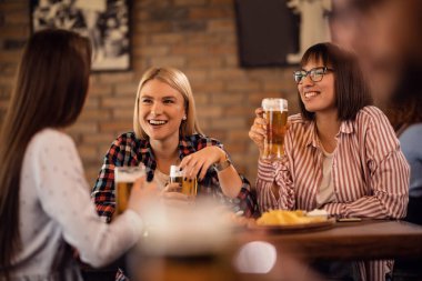 Young happy women having fun while communicating and drinking beer in a tavern. 