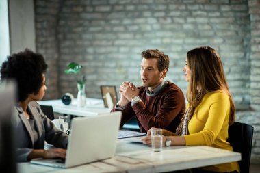 Smiling couple having a meeting with African American bank manager and talking in the office. Focus is on man.