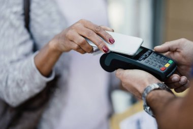 Close-up of woman using smart pone while making contactless payment to a delivery man. 