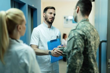 Army soldier handshaking with a doctor in a lobby at clinic. Focus is on doctor. 