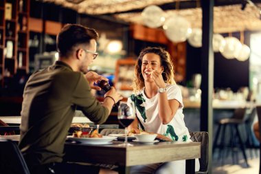 Young couple enjoying in a lunch time in a bar. Focus is on woman eating her food while man is using pepper mill. 