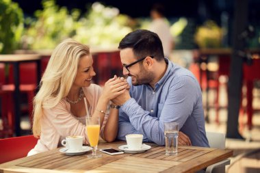 Happy couple holding hands while sitting close to each other and communicating in a cafe. 