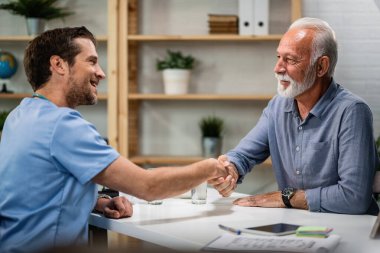 Happy doctor greeting and handshaking with senior patient at his office. Focus is on senior man. 