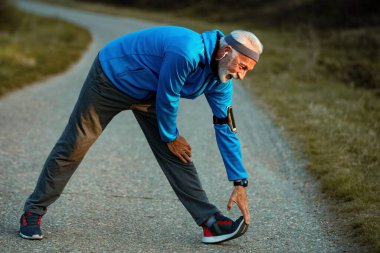 Mature sportsman warming up before the run and stretching on the road in nature. 