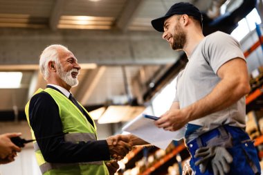 Low angle view of happy senior businessman handshaking with male employee while visiting industrial building. 