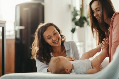 Young happy mothers having fun while playing with a baby at home.